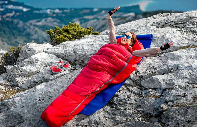 a young girl sleeping over mommy style sleeping bag in a top of mountain