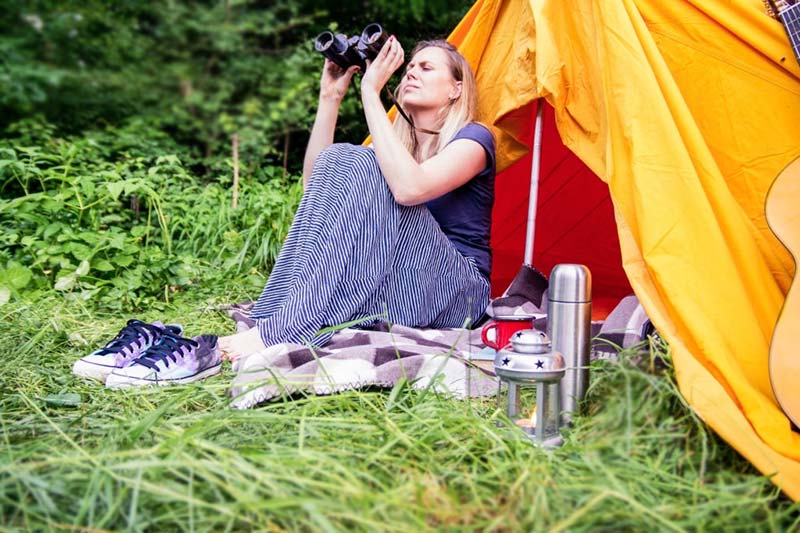 Female-camper-looking-through-binoculars-while-sitting-in-tent